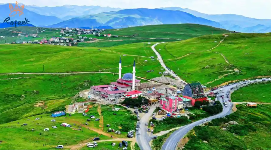 منظر طبيعي بانورامي لبحيرة أوزنجول في طرابزون يوضح الأكواخ الخشبية والجبال الخضراء المغطاة بالضباب أثناء رحلات السياحة في طرابزون.